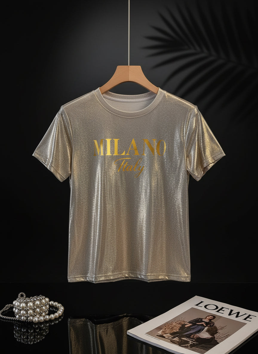 A sparkling champagne golden graphic t-shirt with 'MILANO Italy' printed on the front, displayed on a beige background.
