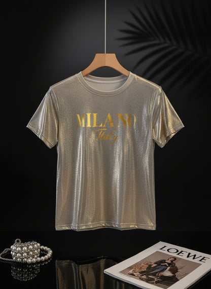 A sparkling champagne golden graphic t-shirt with 'MILANO Italy' printed on the front, displayed on a beige background.