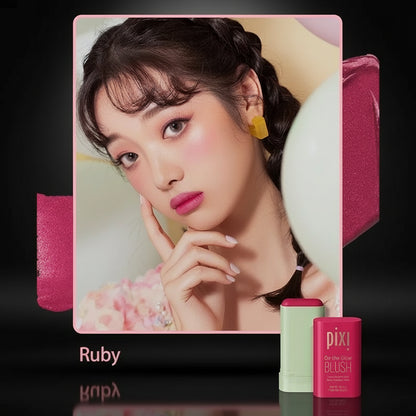 A woman with a pink blush on her cheeks, holding a pixi beauty blush stick with the shade 'Ruby' displayed alongside.