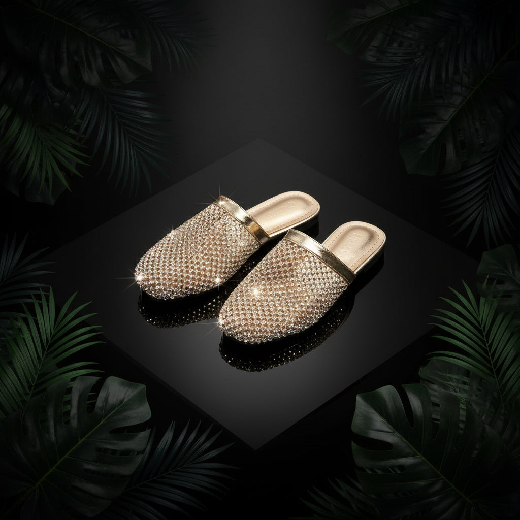 A pair of gold-colored flat slippers adorned with sparkling rhinestones, displayed alongside a pair of blue denim jeans, with the slippers resting on a reflective surface.